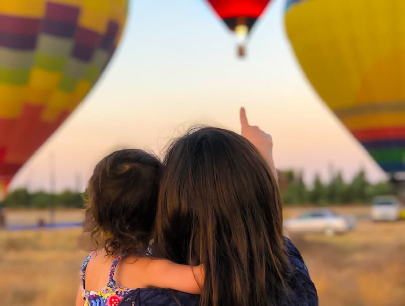 mother pointing out towards air balloon holding her baby